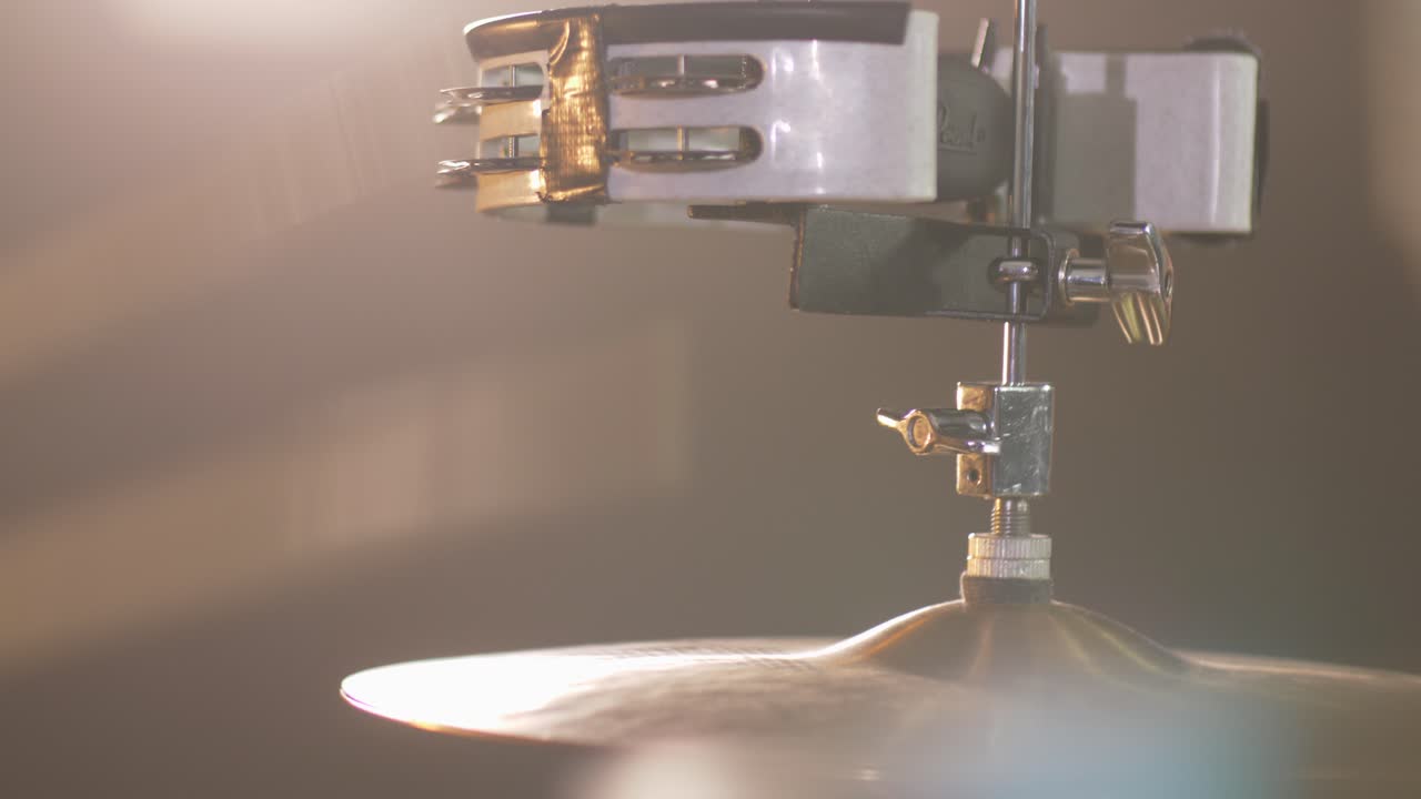 Close up of a Hi-Hat drum with a tambourine, while a drummer plays with sticks a fast rythm with a warm led light in the bckground