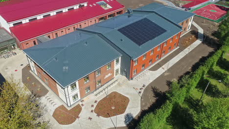 Toma-Aérea-Ascendente-Del-Edificio-Con-Paneles-Solares-En-Letonia-Y-Campo-De-Fútbol-Durante-El-Día-Soleado