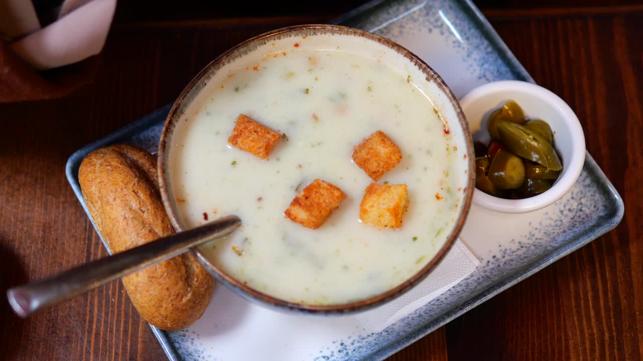 un plato de sopa cremosa con croutons y un lado de pan