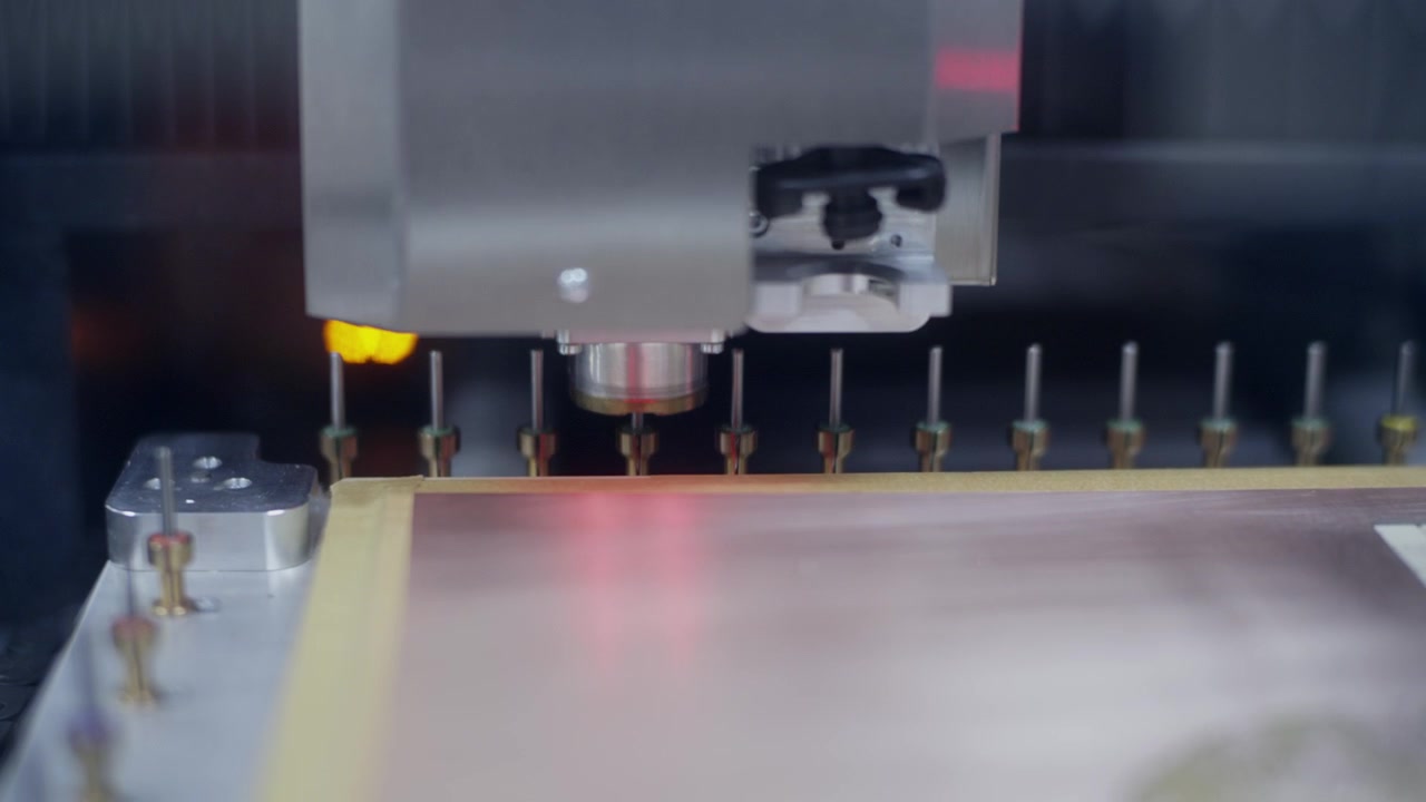 Close-up de um fuso de máquina de roteamento CNC automatizada posicionado sobre uma placa de cobre em branco para fabricar uma placa de circuito impresso, com brocas em segundo plano.