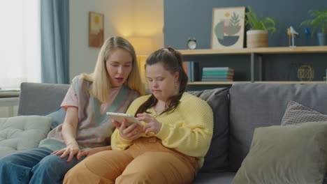 woman and girl with down syndrome using tablet and speaking at home