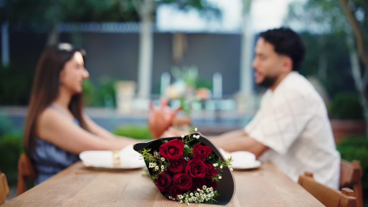 Coppia romantica ad un appuntamento che si tiene per mano, con rose rosse sul tavolo