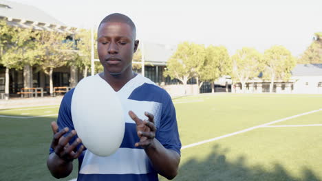 holding rugby ball, african american male athlete in standing on sports field, copy space