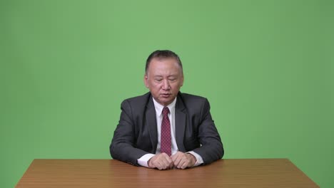 성숙한 일본인 사업가들이 초록색 배경에 대해 이야기하고 있습니다.