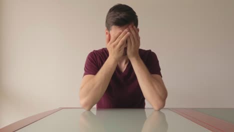 young man sitting at table and stuggling to make a decisive choice, medium close-up still shot indoors