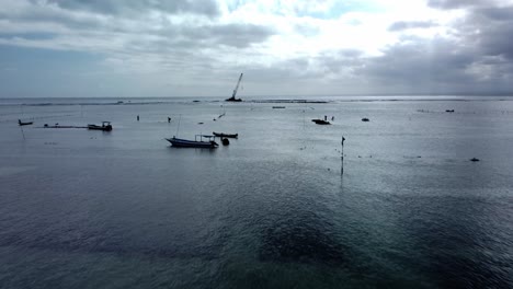 Aerial-dolly-shot-over-the-sea-near-Nusa-Lembogan-with-a-view-of-the-crane-shipwreck-in-calm-waters-with-single-boats-and-locals-in-the-water-during-an-exciting-trip-through-bali,-indonesia