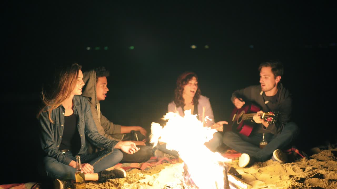 즐거운 젊은이 들 이 밤 늦게 불  ⁇  에서 노래 를 부르고, 기타 를 연주 하고, 맥주 를 마시고, 즐거운 친구 들 이 이야기 하고 재미 를 느끼고 있다