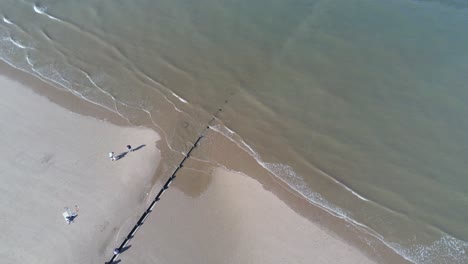 tourists walking on sunny aerial view looking down over golden sandy beach tide