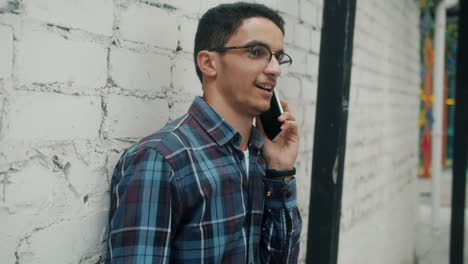 young man talking on phone by brick wall