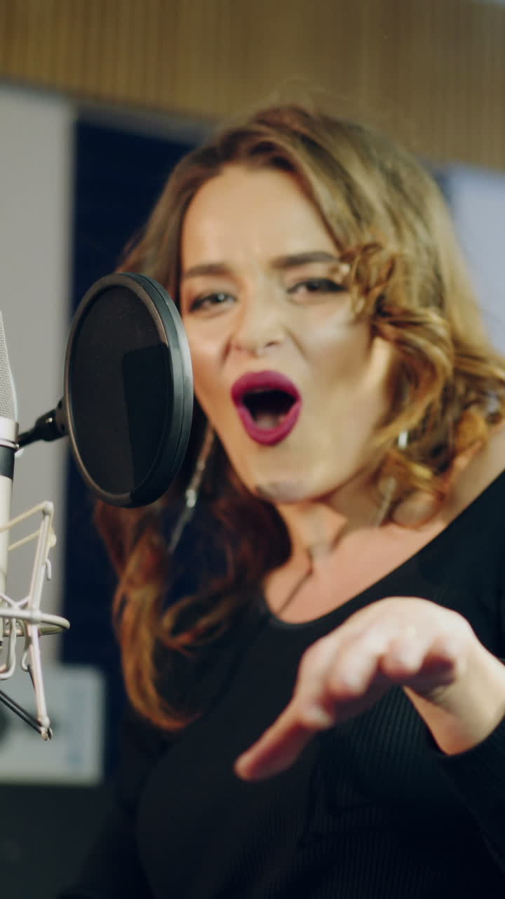 Young female singer recording album in the professional studio. Woman singing a song in music recording studio. Vertical video