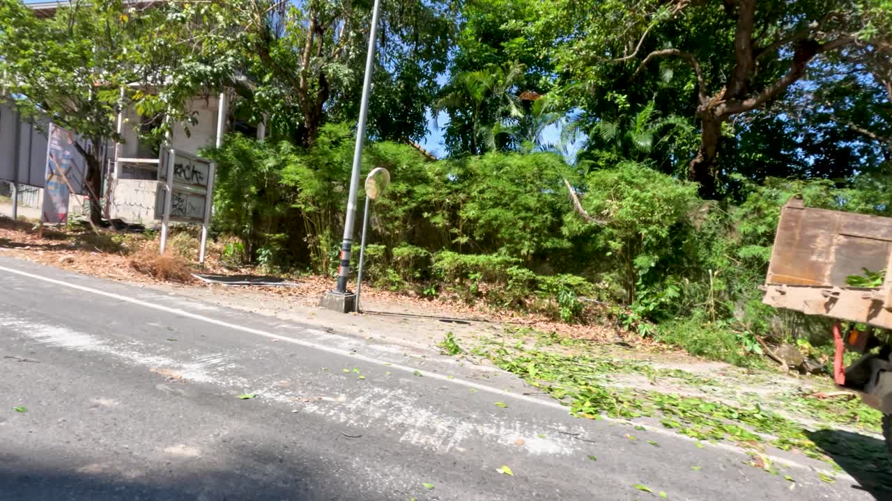 Excavator and dump truck operate on sunny roadside, workers manage traffic, camera pans construction activity
