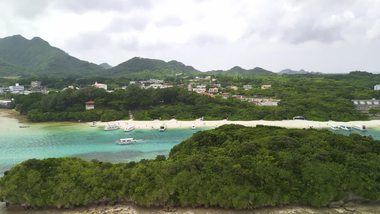 Ripresa con drone delle acque turchesi e delle sabbie bianche della Baia di Kabira, con barche turistiche e isole verdi lussureggianti sotto un cielo nuvoloso a Okinawa