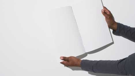 Video-of-hand-of-african-american-man-holding-book-with-blank-pages,-copy-space-on-white-background