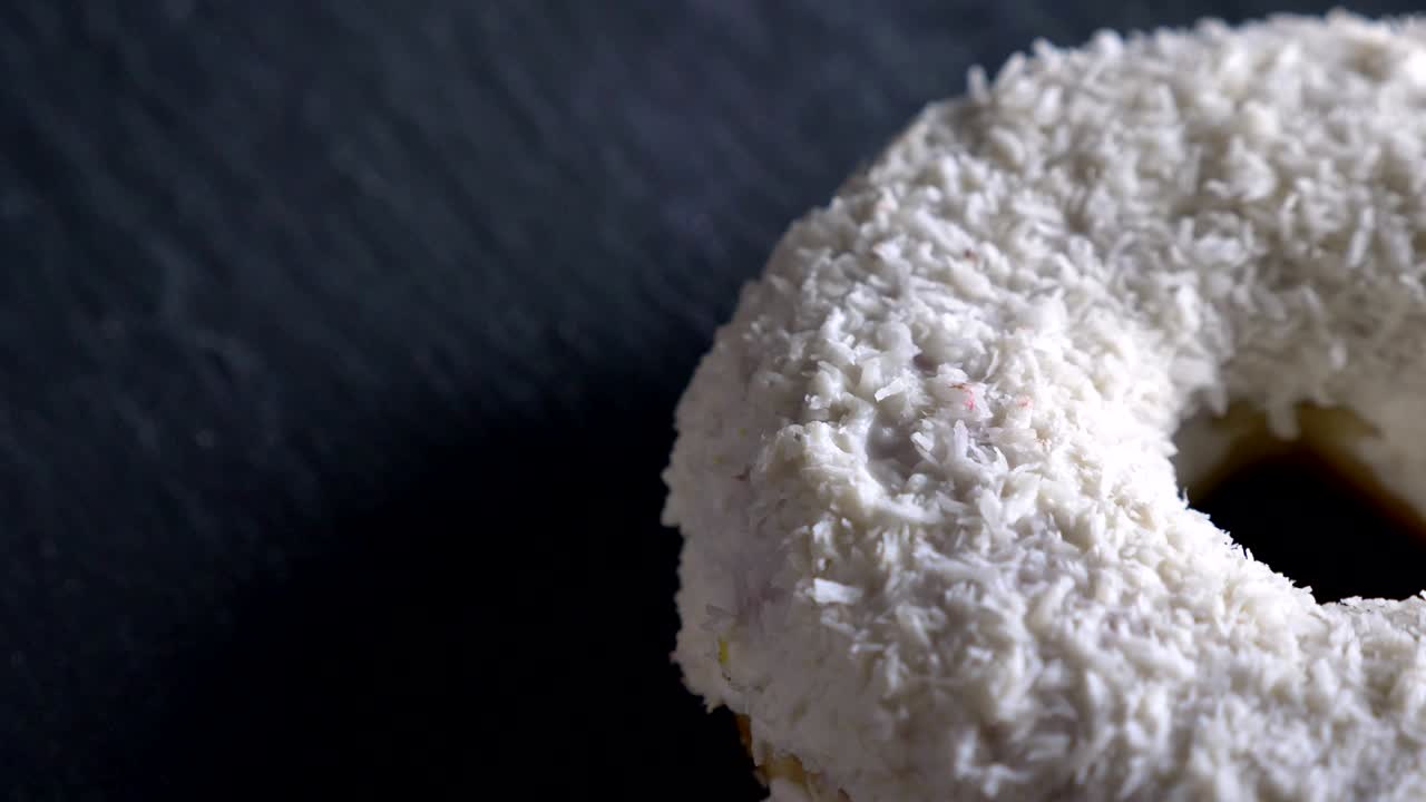 un primer plano de una deliciosa rosquilla blanca con papas fritas de coco girando lentamente sobre el fondo gris de la mesa.