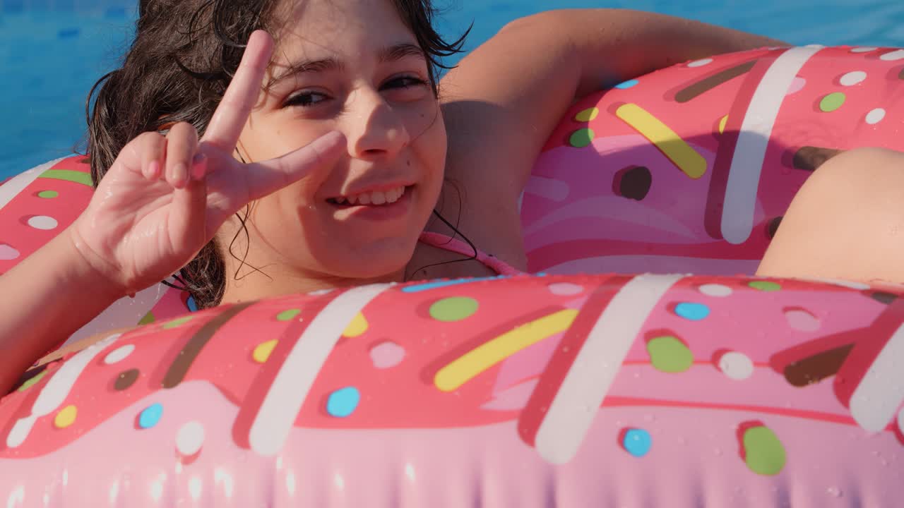 11-12 años feliz chica caucásica linda acostada en un círculo de rosquilla inflable en la piscina en un jardín. vacaciones de verano frescas para niños y niños. juegos en el agua. donat rosa. 4k cámara lenta