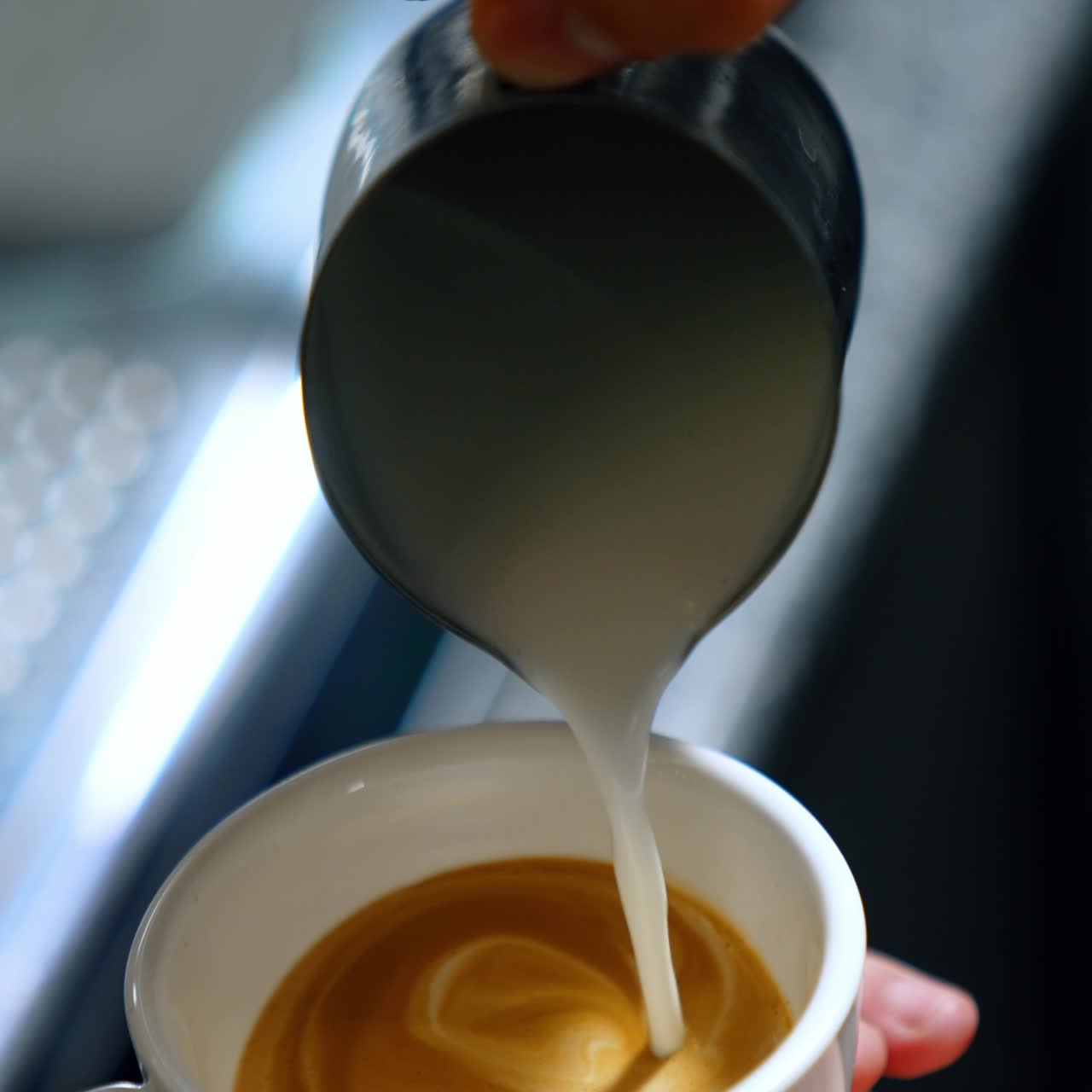 Mani maschili tengono una tazza di caffè bianca riempiendola di latte. Un barista prepara una bevanda al latte. Primo piano. Schermo verticale. Sfondo sfocato.
