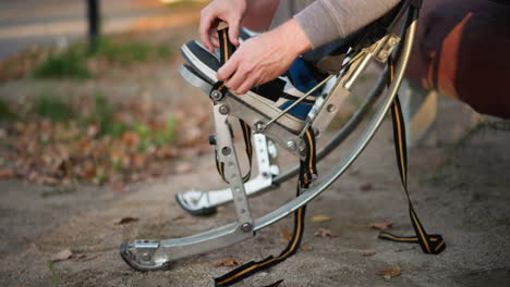 close-up of person adjusting spring stilts on gravel path with fallen leaves, wearing gray sweatpants and dark sneakers, ground-level focus on preparation and equipment setup outdoors