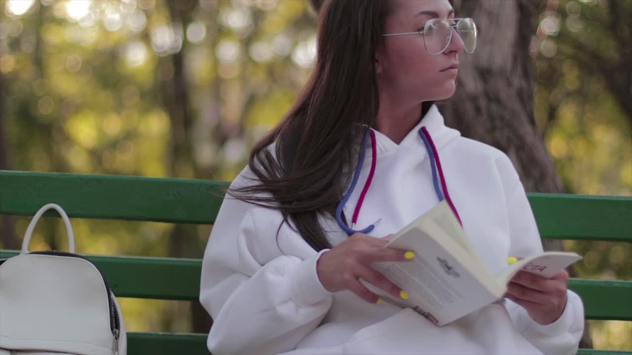chica con gafas leyendo un libro en un banco en un ambiente tranquilo en un parque