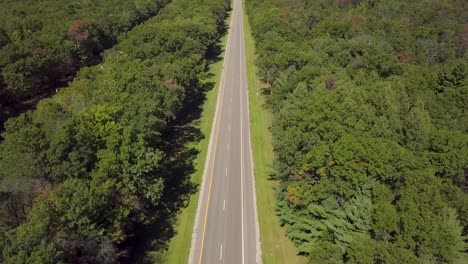 daytime clip of an empty michigan asphalt highway in rural america, in sunny summer conditions with green trees and scenic aerial view