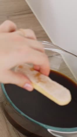 close-up of female hands dipping ladyfingers in coffee and placing them on cream for tiramisu.