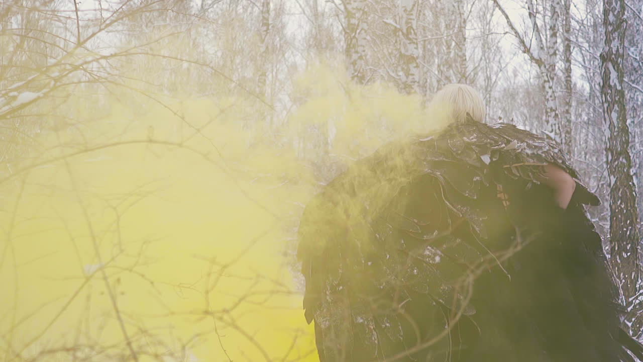 피닉스 의상을 입은 모델이 노란 연기 뒷면을 걷고 있습니다.