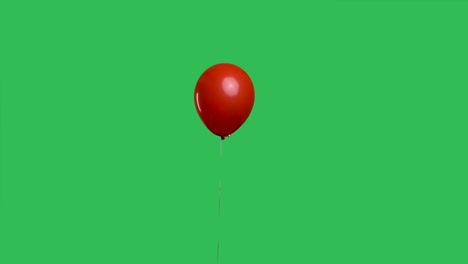 red oval shaped balloon hanging in the air against the background of a green screen chroma key. colorful helium balloon. birthday, party decoration, holiday, surprise, gift. slow motion