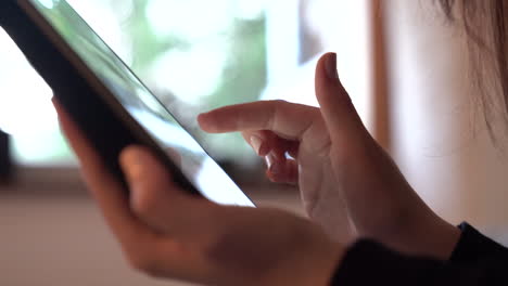 handheld closeup side shot of a woman's hands using a tablet scrolling on touch screen