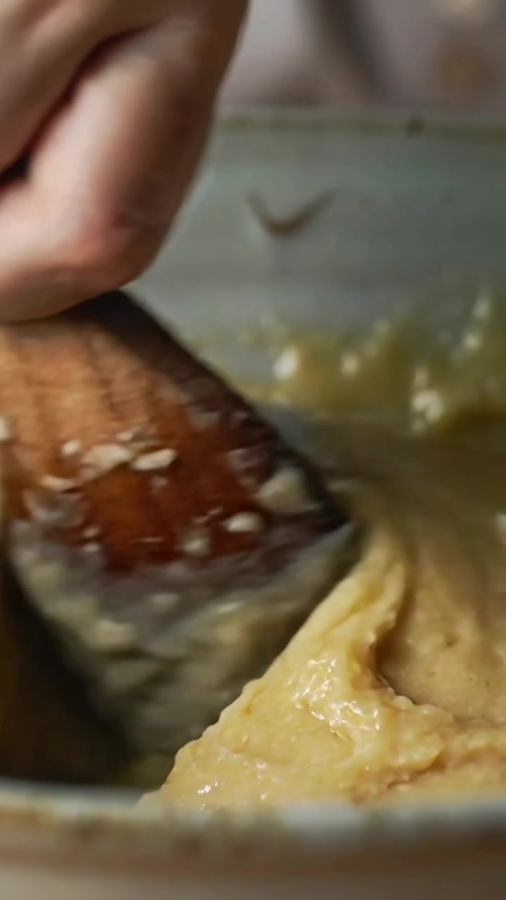 Vertical video: Pressing wooden spatula into lumpy batter, hands scraping and smoothing at counter