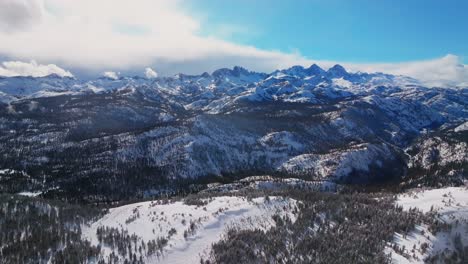 minarets jagged towering peaks summit vista panoramic landscape aerial drone winter mammoth mountain ski resort california inyo national forest the hemlocks sunny blue skies cloudy backwards pan up