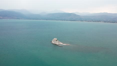 Foto-Panorámica-Del-Castillo-De-Bourtzi-En-Medio-Del-Agua-Con-Montañas