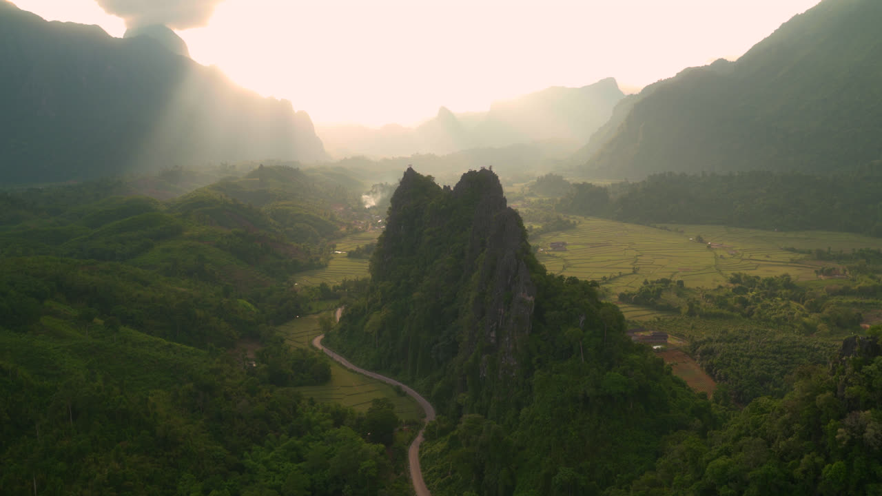 Mountain peaks rise above misty valleys near Vang Vieng creating calm serenity, sparkling soft daylight, static backdrop