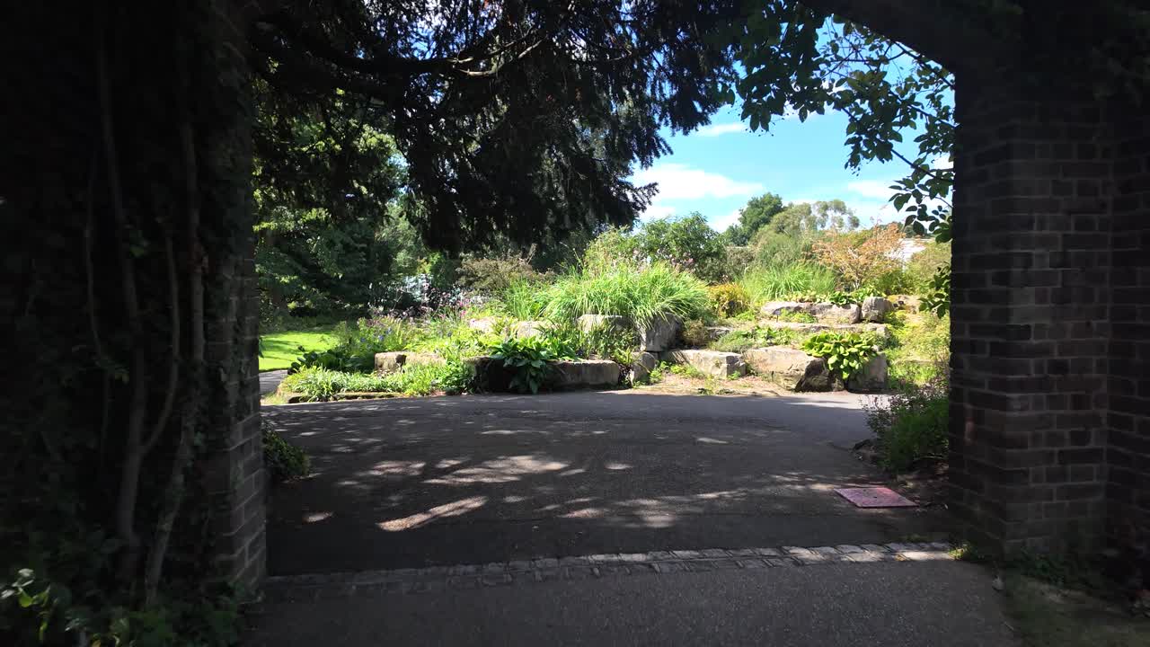 静かな公園で、ツタで覆われたアーチ道を抜ける平和な庭の小道を日光が照らす。POV。