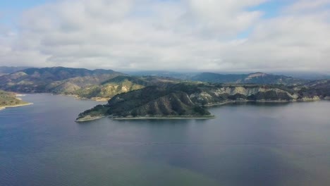 Mountains-and-lake,-covered-with-trees,-under-a-blue-sky-with-clouds-camera-pan-right