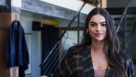 retrato de una mujer sonriente dueña de una tienda de moda de pie frente a una exhibición de ropa