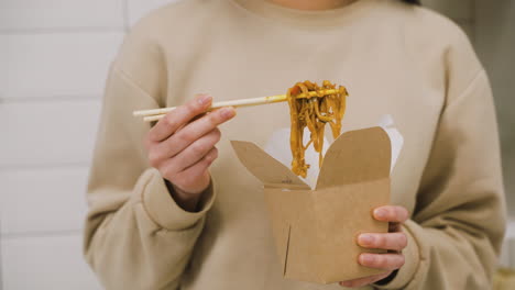 close up view of a woman holding japanese chopsticks while eating ramen in the kitchen