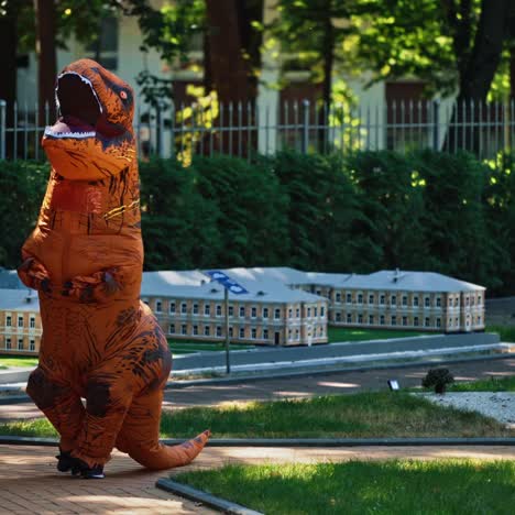 cartoon animation. dragon costume in small city. person wearing blow-up animal suit walking among beautiful handmade architecture in the park.