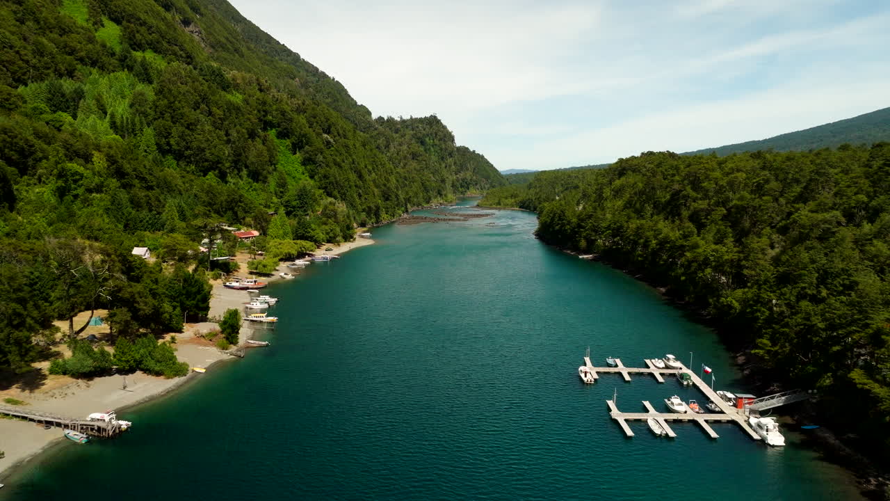 Aerial footage captures Petrohué Port on Lago Todos Los Santos in Chile. Surrounded by forested hills, the deep blue lake and docks create a tranquil and scenic natural retreaI