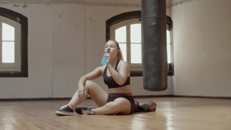 long shot of woman drinking water after boxing workout in gym