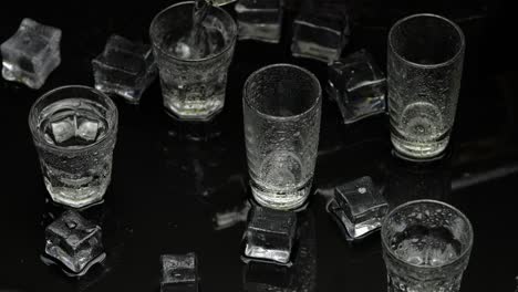Barmann-Gießt-Gefrorenen-Wodka-Aus-Der-Flasche-In-Ein-Schnapsglas.-Eiswürfel-Vor-Dunklem,-Nassem-Schwarzem-Hintergrund