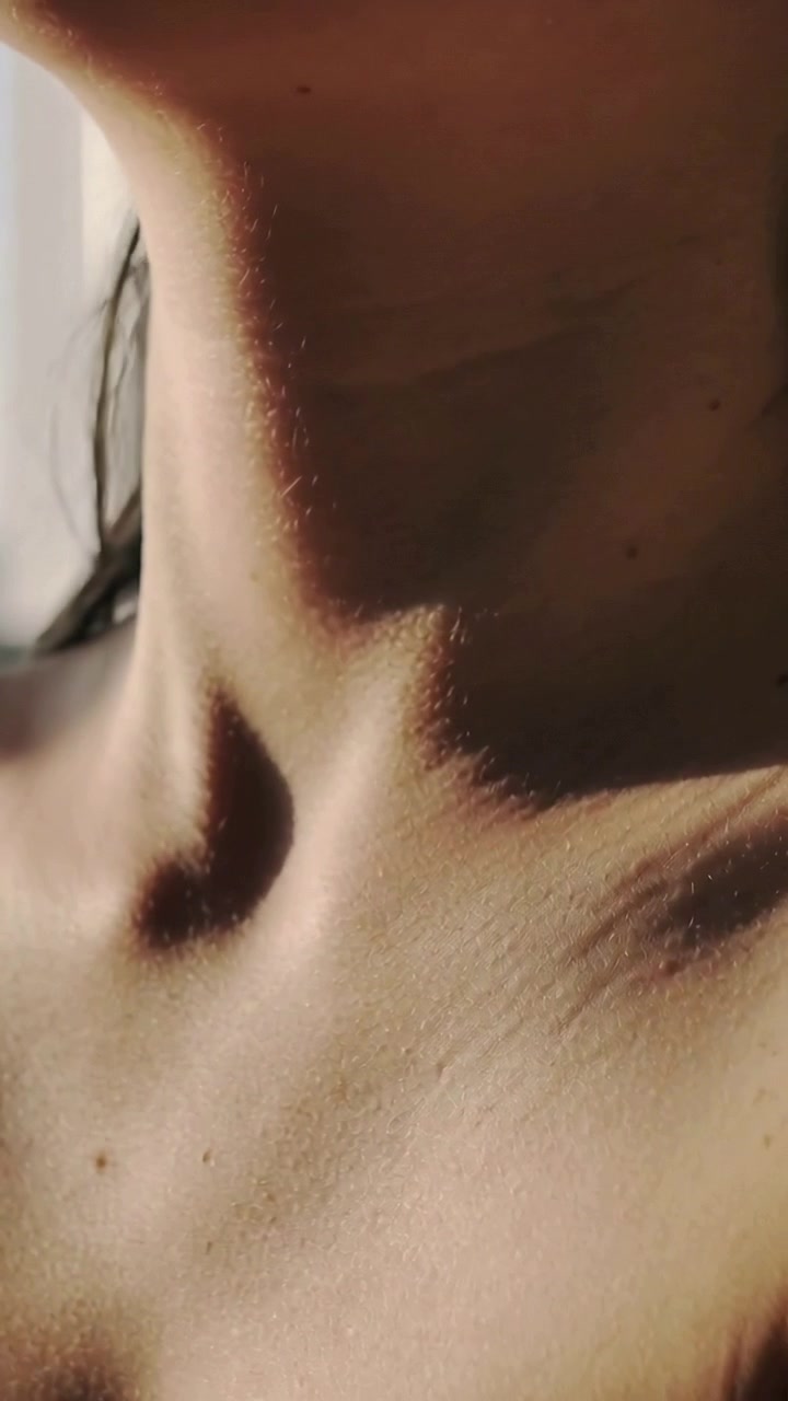 Video verticale: Testa di donna inclinata in alto a sinistra verso la luce della finestra, esponendo clavicola e spalla.