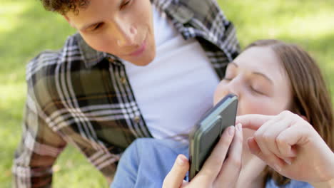 Happy-diverse-couple-having-picnic-and-using-smartphone-in-sunny-garden,-in-slow-motion