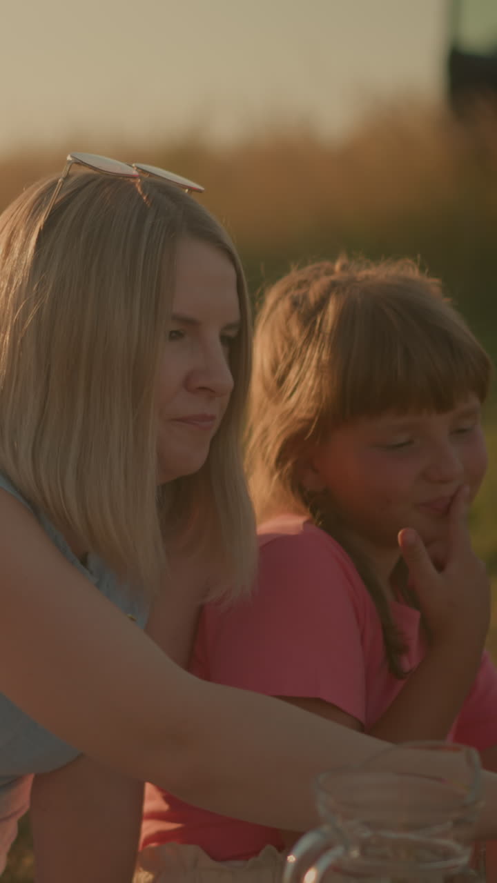 중년 여성이 밖에서 물을 마시며 어머니와 딸 에 앉아있는 부분적인 모습, 어머니는 녹색 포도에 손을 고 먹고, 딸은 미소 짓고 있습니다.