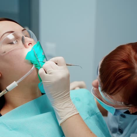 woman in chair at stomatology clinic. professional female dentist in protective mask and glasses treating patient's teeth using medical equipment.