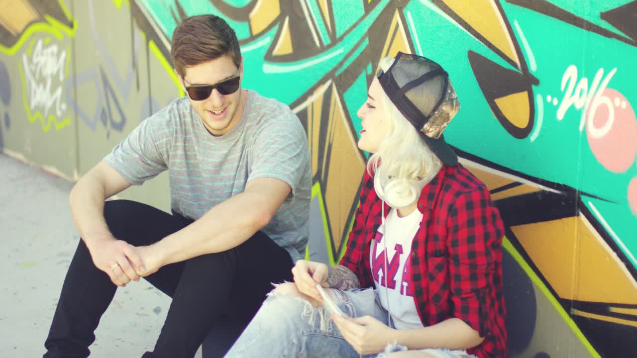 pareja hipster relajándose contra una pared de graffiti