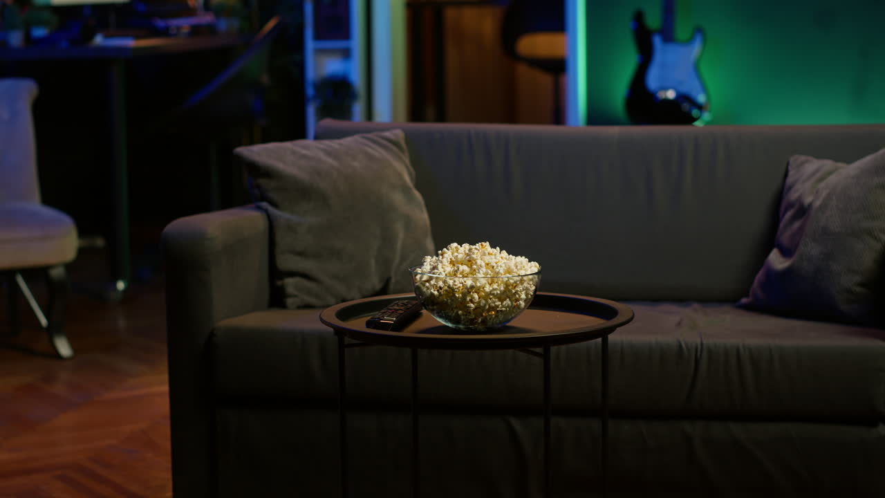 uma tigela de pipoca na mesa ao lado do controle remoto em um apartamento iluminado a neon
