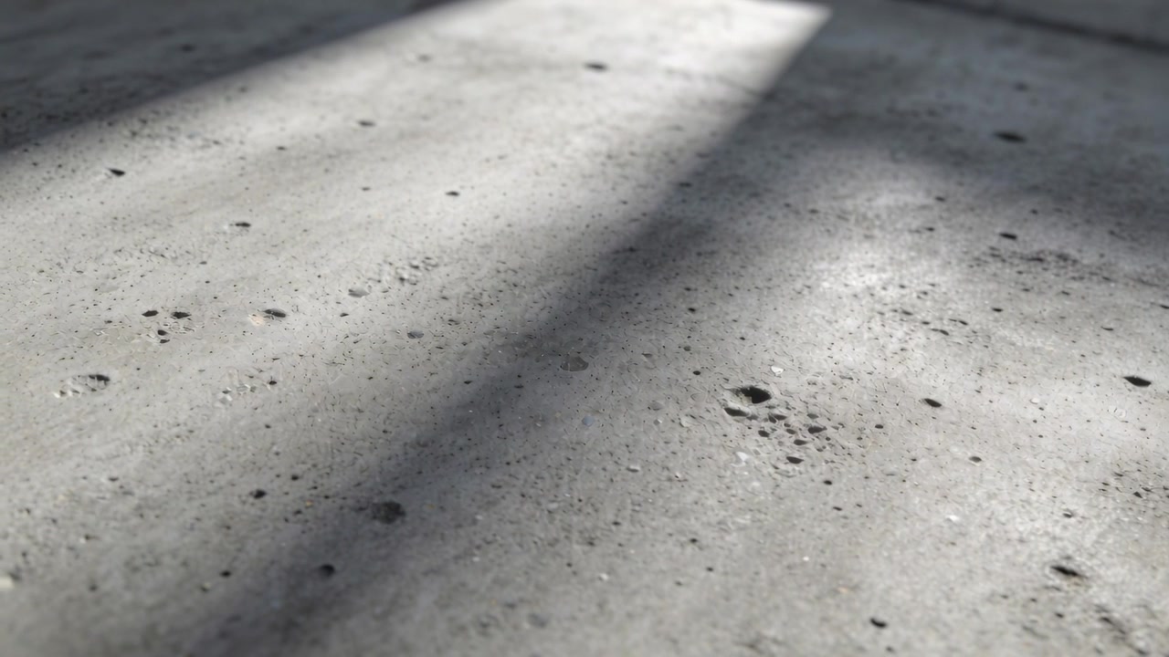 Streaming sun from slats shifting shadows over concrete floor in workshop bright strip pocks grit