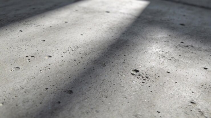 Streaming sun from slats shifting shadows over concrete floor in workshop bright strip pocks grit
