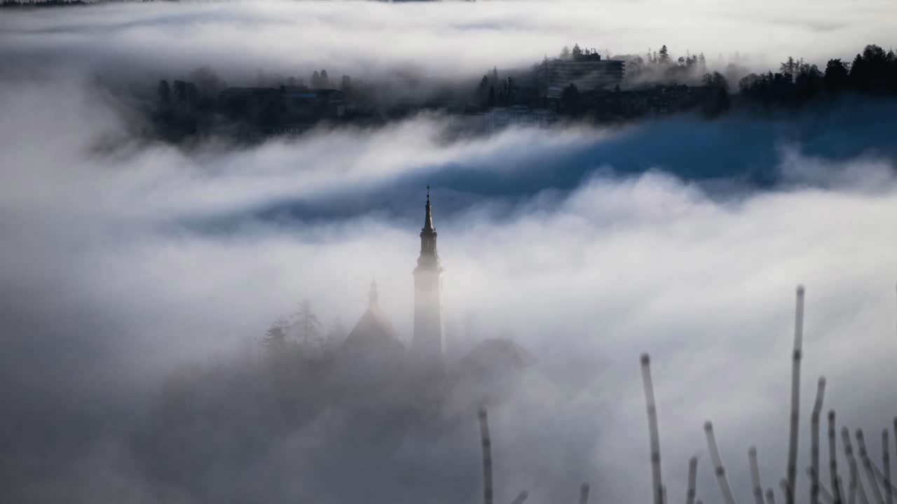 Time lapse of church in Bled Slovenia with fog going  over the building captured from a hill called Ojstrica with a telephoto at winter time in the morning