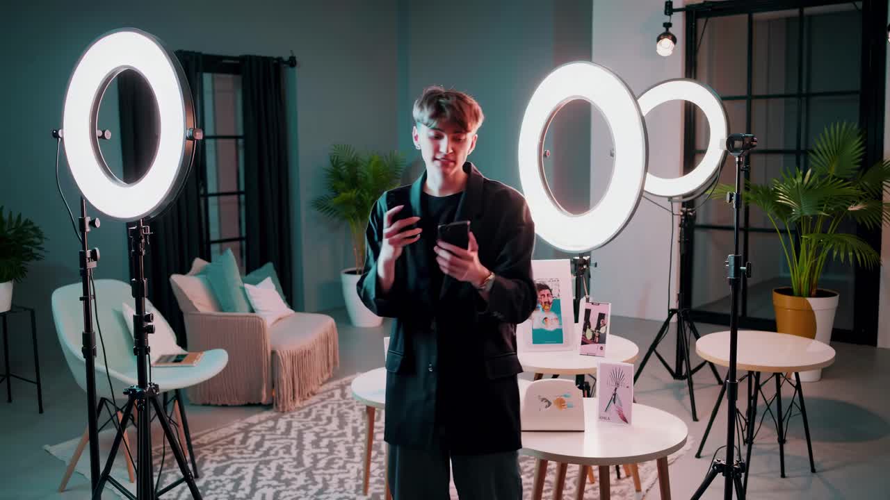 A video shoot setup with a young man holding a phone, surrounded by ring lights