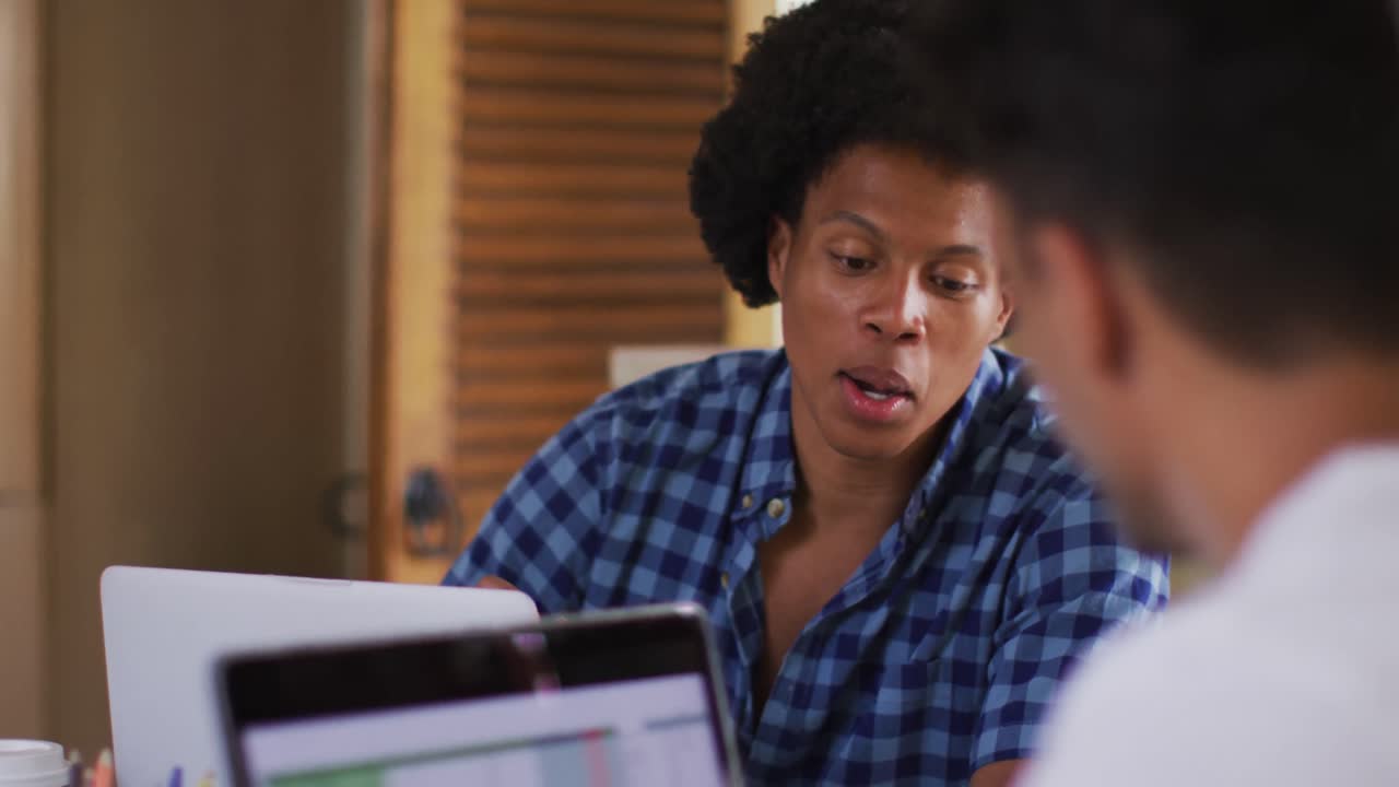 Two diverse male friends in kitchen with laptop and talking